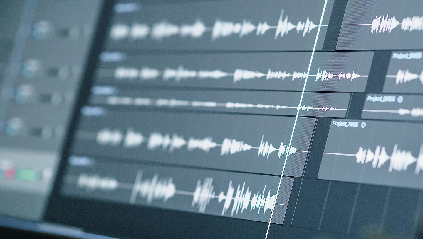 Close-up of digital audio editing software showing multiple audio tracks with white waveforms on dark timeline interface