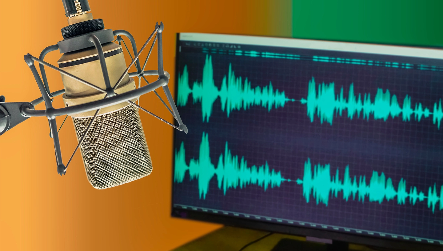 Studio condenser microphone on shock mount against orange background with audio waveform display on monitor showing green frequency visualization
